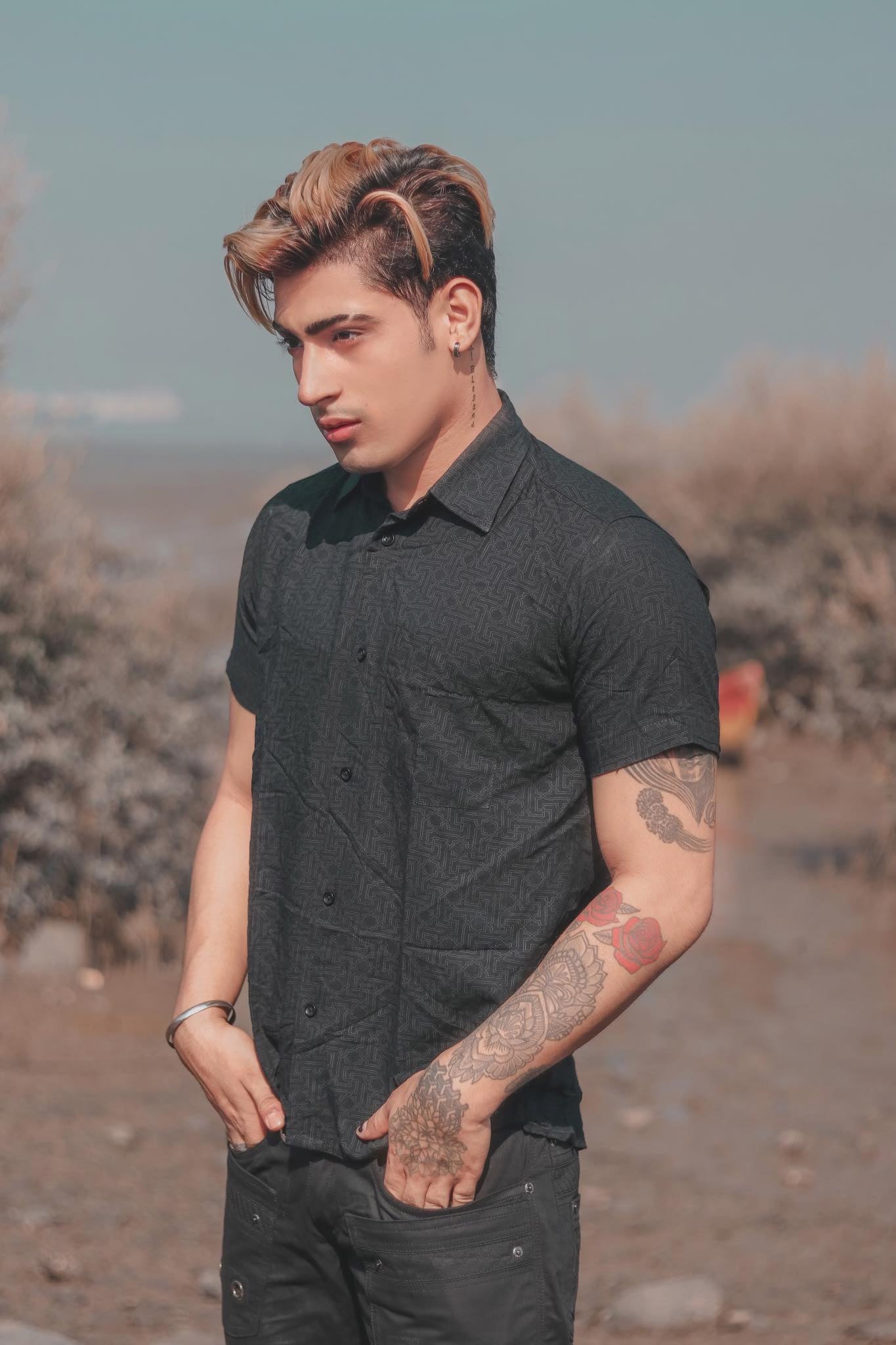 A man wearing a black short sleeve geometric print shirt with the collar buttoned up, standing outdoors.