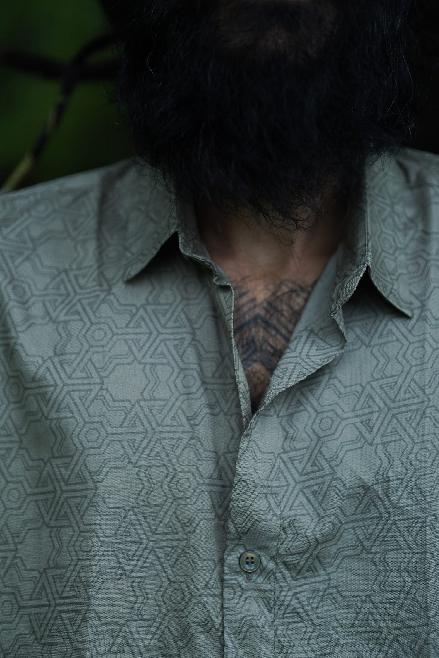 A close-up of a man wearing a short-sleeved, geometric patterned shirt in an outdoor setting.