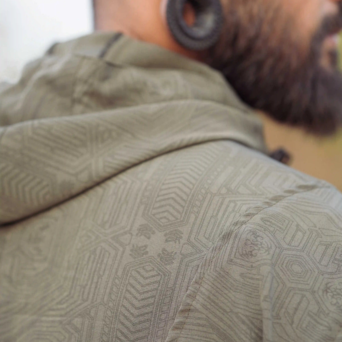 Khaki geometric windbreaker jacket close-up showing detailed Metanoia pattern on shoulder