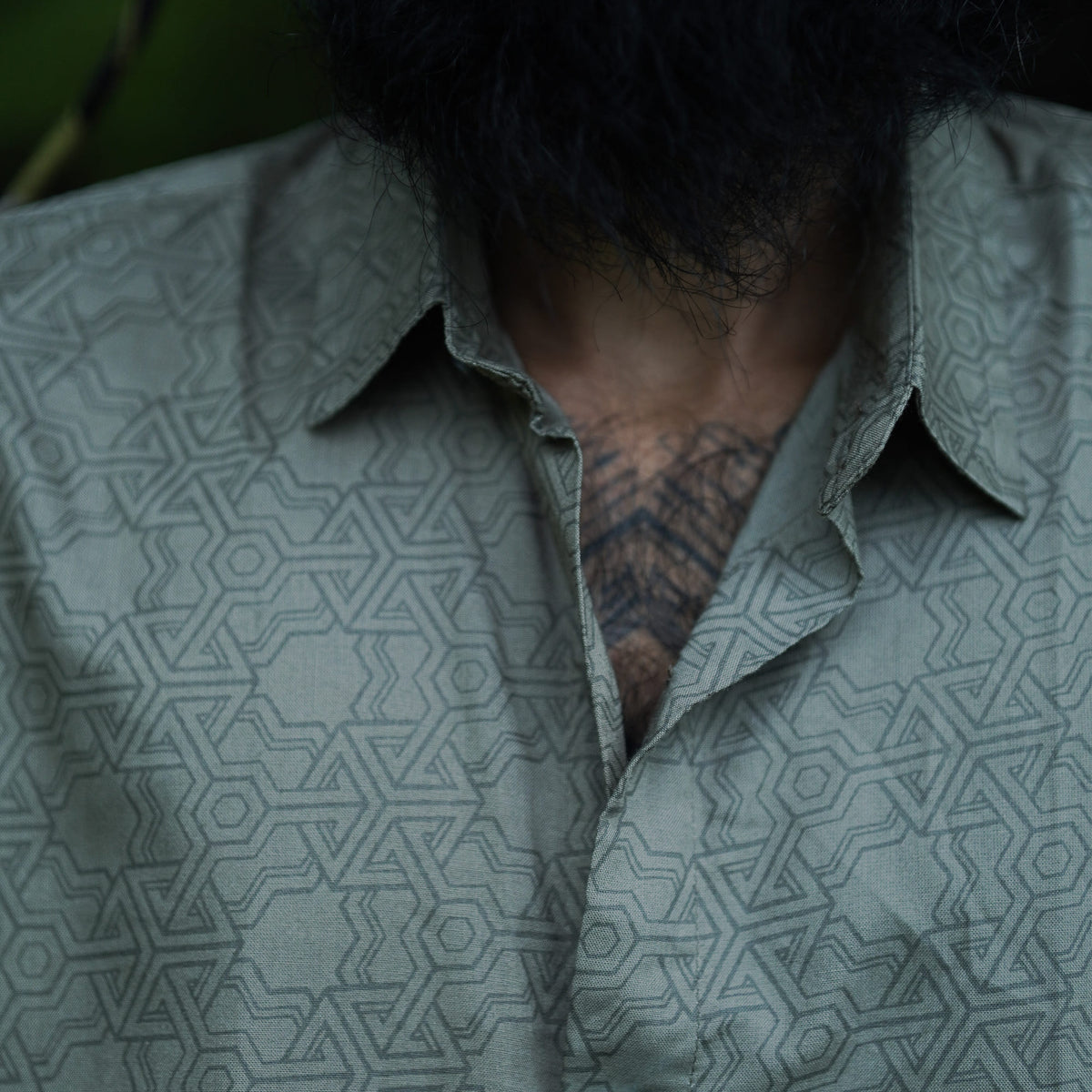 A close-up of a man wearing a short-sleeved, geometric patterned shirt in an outdoor setting.