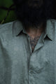 A close-up of a man wearing a short-sleeved, geometric patterned shirt in an outdoor setting.