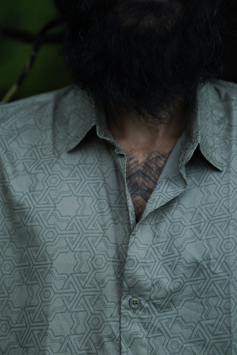 A close-up of a man wearing a short-sleeved, geometric patterned shirt in an outdoor setting.