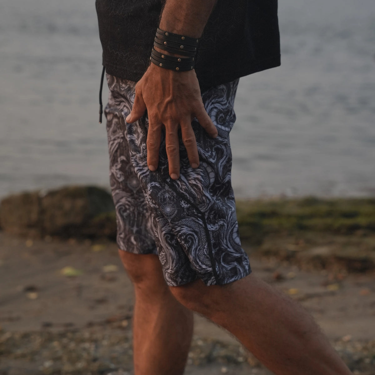 Abstract Dragon psychedelic board shorts for men with monochrome dragon print, shown from the side at the beach.
