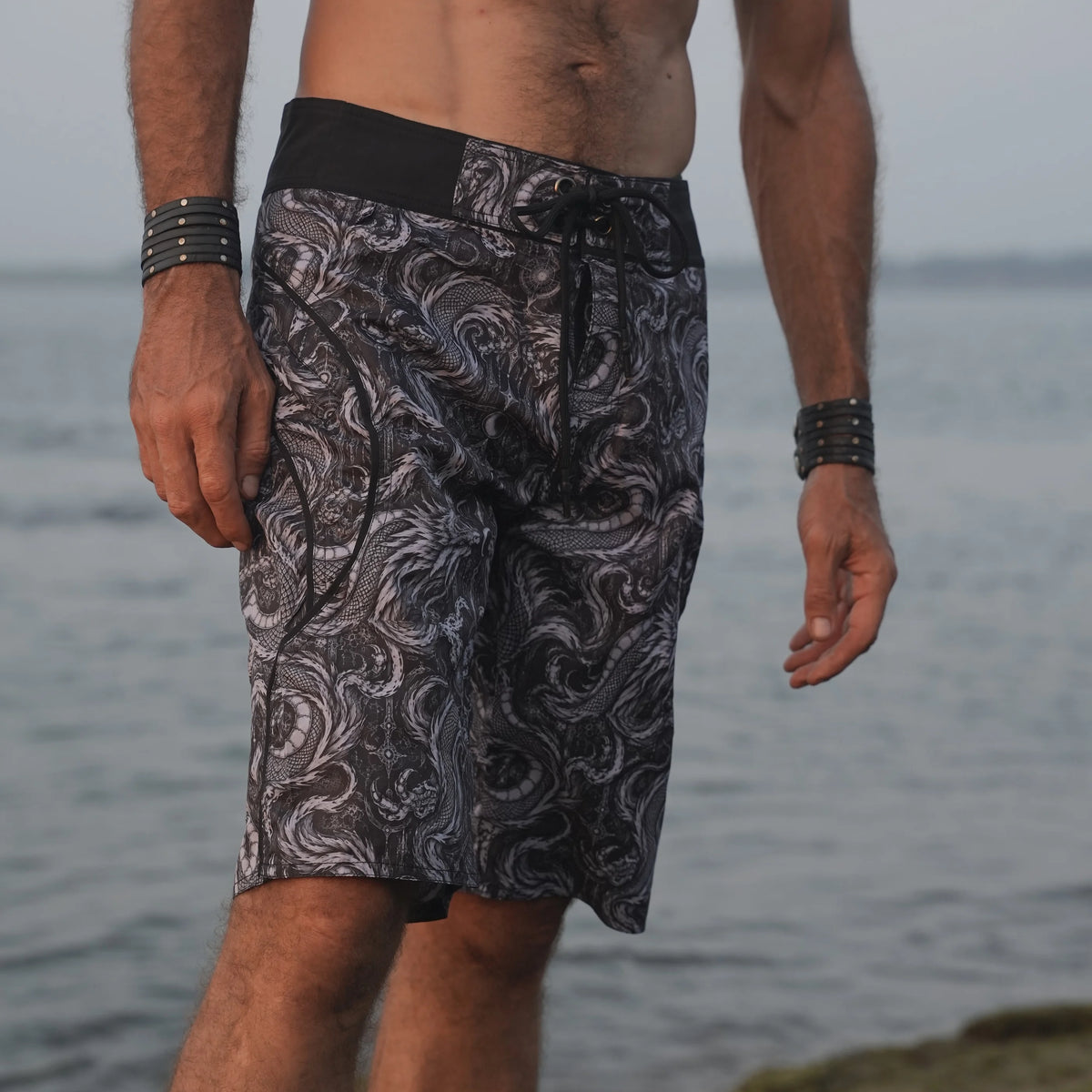 Front view of men's Abstract Dragon board shorts with an intricate monochrome dragon print and contrasting black drawstring waistband.
