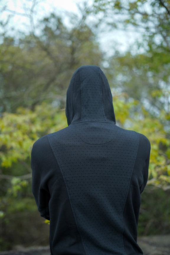 Model wearing the Clover Vortex black hoodie with a full-length of back side patterned panels
