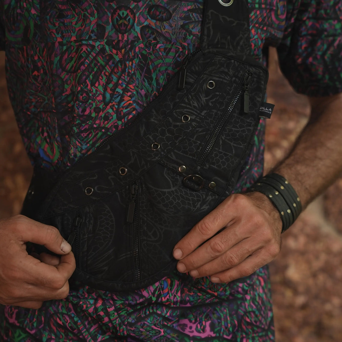 Vanta Dragon crossbody bag held in front, showing its dark artwork and multiple zippered compartments