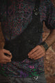 Vanta Dragon crossbody bag held in front, showing its dark artwork and multiple zippered compartments